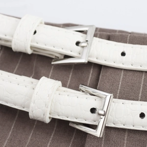 White faux crocodile leather belts with silver square metal buckles on striped trousers