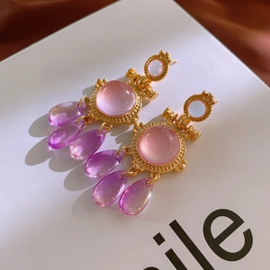 Detail of vintage gold tassel earrings with pink gradient resin drops on silk fabric
