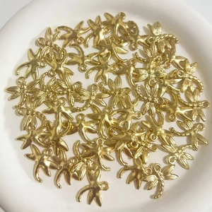 Bulk gold plated ABS dragonfly pendants for DIY jewelry making displayed on a white plate