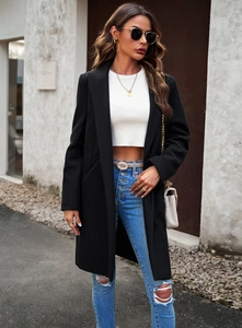 Detail of a minimalist black mid-length wool coat worn open with a casual outfit