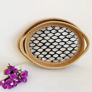 Close-up of handmade oval rattan trays featuring intricate shell mosaic patterns in base