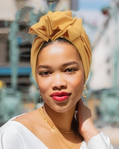 Close-up of mustard yellow fabric turban hat paired with gold hoop earrings and necklaces