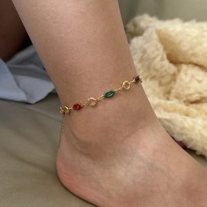 Golden ankle bracelet with colorful lip and ring charms worn on ankle for fashion look