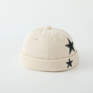 Detail of cream corduroy beanie featuring black star embroidery and ribbed knit texture