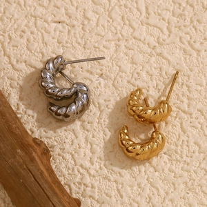 Close-up of gold and silver twisted horn earrings on a textured cream background