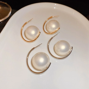 Fashionable C-shaped gold and silver earrings with faux pearl on a ceramic tray