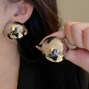 Close-up of oversized metallic orb earrings with mirror finish and ribbed texture
