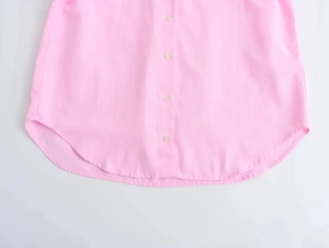 Detail of pink cotton shirt showing curved hemline and pearlized buttons in a close-up
