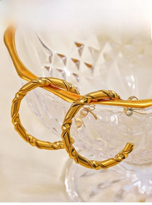 Detailed macro view of 18K gold plated C-shaped twisted hoop earrings on glass