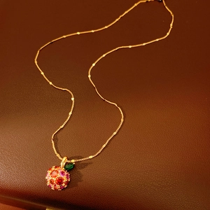 Close-up of 14k gold plated apple pendant with red pavé zircons on leather background