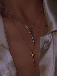 Detailed view of silver and gold nail pendant necklaces on model with silk backdrop