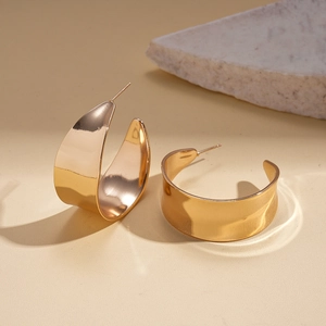 Detail view of gold wide C-shape earrings with a polished metallic finish and smooth surface