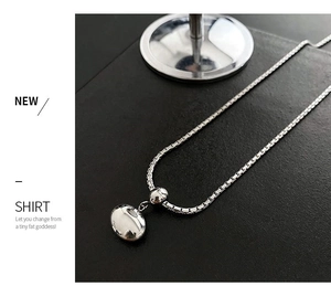 Close-up of polished silver bean pendant on a sleek box chain against a dark textured surface