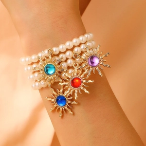 Three-layer pearl bracelet with golden sun pendants and colorful gemstones on a wrist