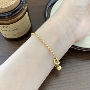 Close-up of a gold beaded knot heart bracelet worn by a model on a warm minimalist background
