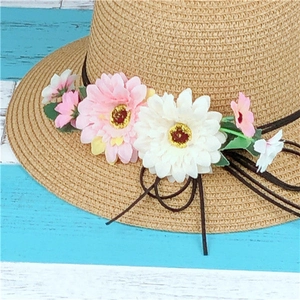 Close-up of woven straw sun hat featuring colorful daisy floral decorations