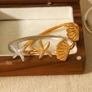 Detailed view of starfish and seashell charms on gold and silver stainless steel bangles