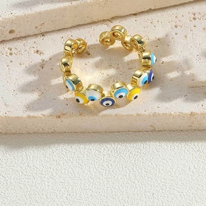 Macro view of gold evil eye ring with colorful enamel details on beige stone layers