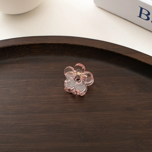 Detail of a transparent pink mini flower hair claw clip on a rustic wooden tray