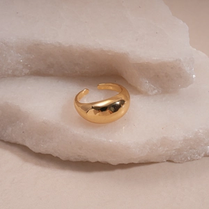 Close-up of a minimalist golden adjustable metal ring on a textured white stone surface