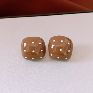 Detail of square brown earrings with white polka dots on a textured leather surface