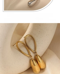 Detailed view of gold teardrop earrings with a polished finish on a soft fabric backdrop