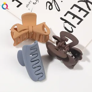 Close-up of three matte hair claws in beige, brown, and grey-blue on a card