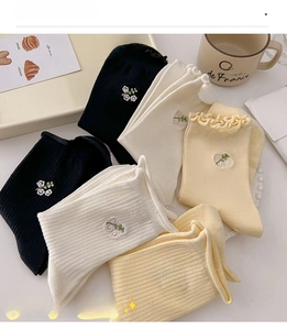 Detail view of ruffled cotton socks with floral embroidery in black and cream colors