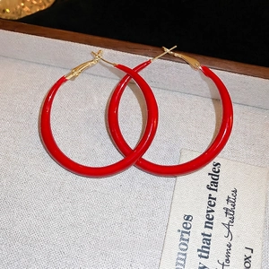 Red enamel hoop earrings with gold-plated hooks on white textured jewelry display tray