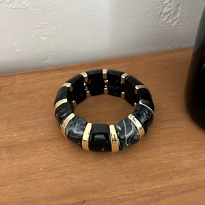 Détail du large bracelet en résine noire avec intercalaires dorés sur bois