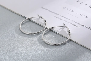 Detail of silver twisted hoop earrings with textured spiral design and metallic finish
