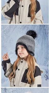 Detail of kids winter knit earflap hat with large faux fur pompom in outdoor snow scene