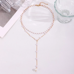 Vue macro d'un collier en Y à deux rangs de perles dorées sur fond blanc élégant