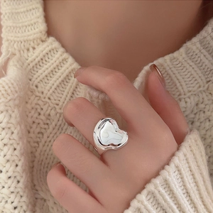 Close-up of a silver heart-shaped ring worn on the finger with a knit background