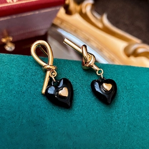 Golden knot earrings with black enamel heart charms displayed on velvet jewelry stand