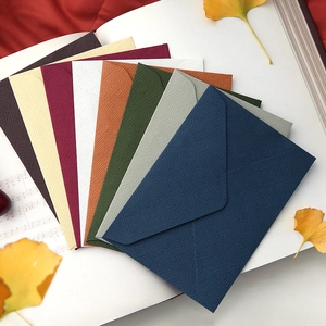 Textured hemp-pattern envelopes in multiple colors arranged on a notebook with autumn leaves