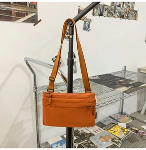Detail of orange nylon crossbody bag featuring front zipper pocket and wide fabric strap