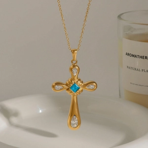 Elegant gold cross necklace with blue square zircon and white teardrop gems on ceramic tray