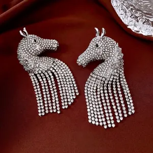 Sparkling silver horse pendant earrings with rhinestone tassels on red satin background