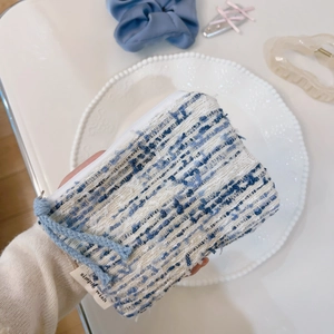 Primo piano della mini pochette in tweed bianco e blu con zip e cordino blu decorativo