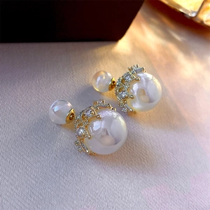 Macro view of gold crown settings with rhinestones on white double pearl stud earrings