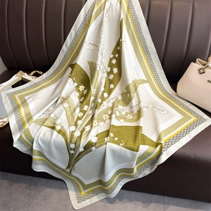 Carré de soie élégant motif muguet drapé sur un canapé en cuir avec un sac à main