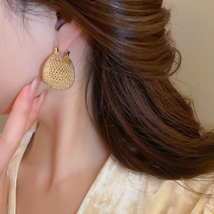Macro shot of gold oval hollow woven earrings on model showing mesh texture detail