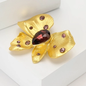 Exquisite gold flower brooch with ruby red gemstone and purple crystals on white pedestal