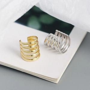 Detailed view of layered C-shape gold and silver ear cuffs on a minimalist book background