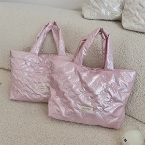 Quilted heart and bow puffer tote bags in pink and white displayed on a soft boucle sofa
