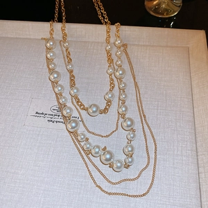 Detailed view of layered faux pearl necklace with gold-tone chains on a textured surface