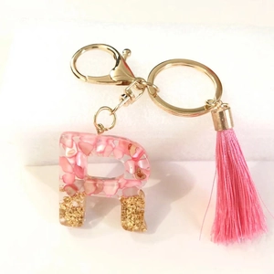 Macro shot of letter R resin keychain with pink shells, gold glitter and tassel