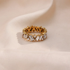 Detailed close-up of a gold ring with rectangular and round clear zircons on beige silk
