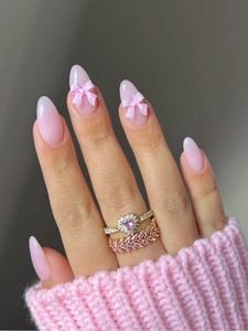 Macro shot of gold heart ring, leaf ring and pink almond nails with 3D bow details
